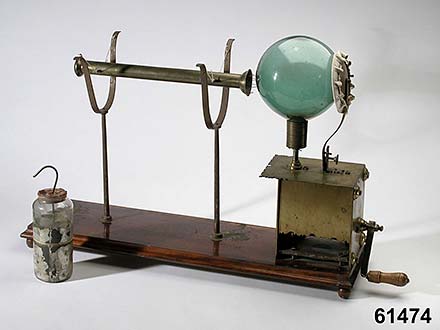 A metal rod is directed towards a glass ball that is standing on a foundation with a crank.