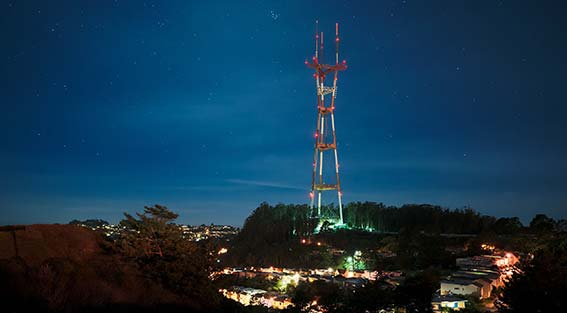 Sutro Tower illuminated at night. Dark blue sky and street lights.